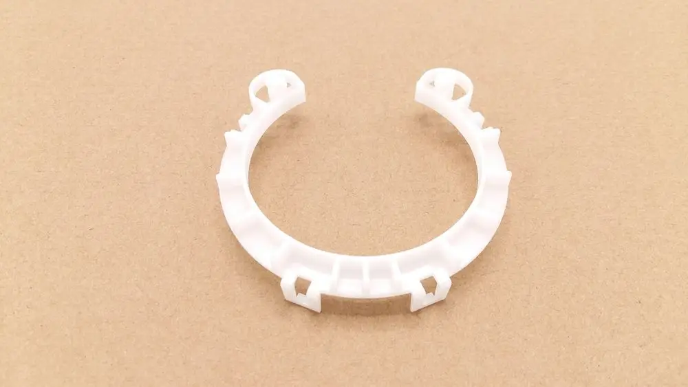 Weißer Kunststoffring mit Montageelementen, geeignet für Remeha Produkte. Der Ring hat eine offene Form und ist auf einem braunen Hintergrund abgebildet.